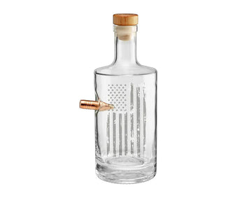 Clear whiskey decanter with a wooden cap and real bullet on a white background from the American brand Benshot available at Spacio retail stores in Mumbai & Kolkata. 