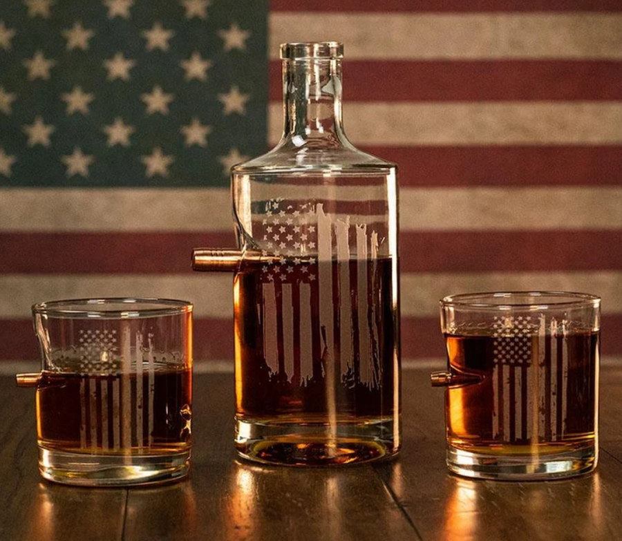 Clear glass whiskey decanter and two whiskey glasses with American flag design against an American flag background from Benshot available at Spacio retail stores in Mumbai & Kolkata. 