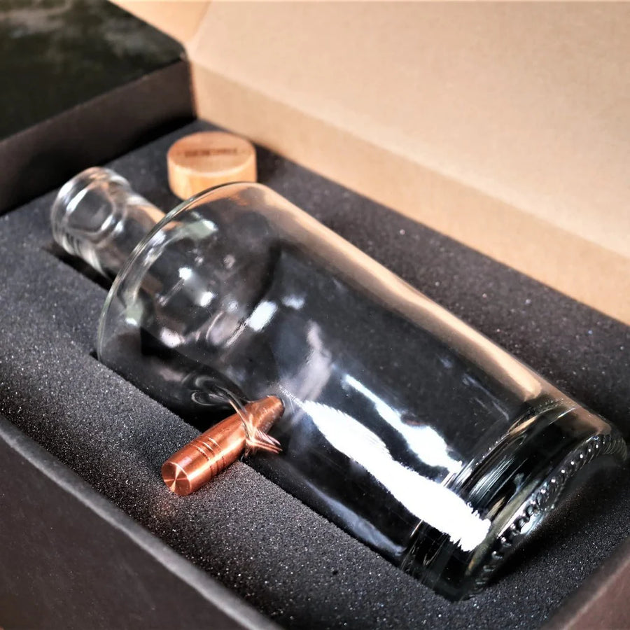 Glass whiskey decanter with a bullet inside, placed in a cardboard box.