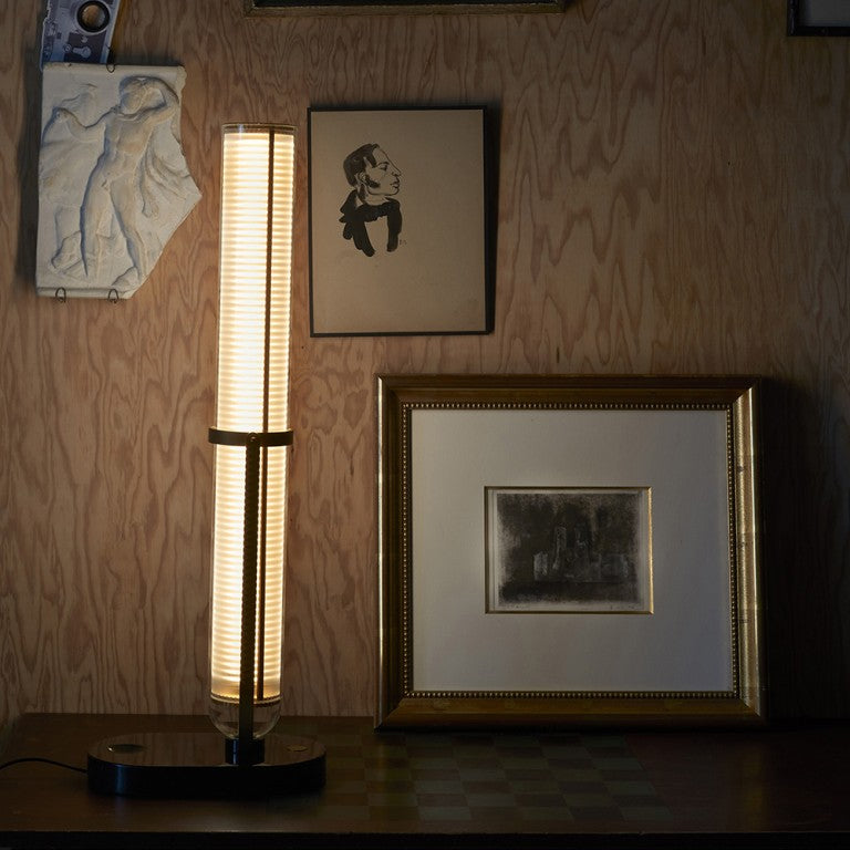La Lampe Frechin table lamp by DCW Editions  upright on a console table with photo frame and art works on wall. 