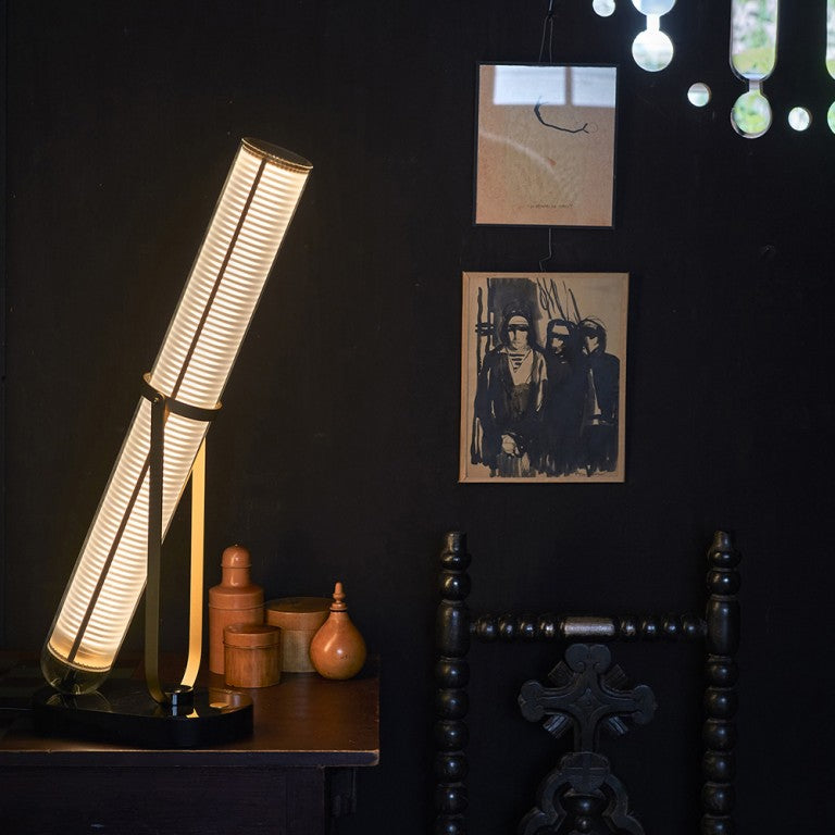 La Lampe Frechin table lamp by DCW Editions  on a side table in a dark theme interior. 