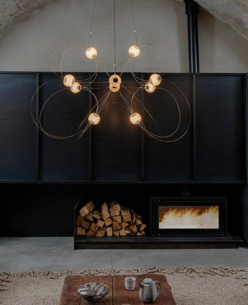 Modern chandelier hanging above a fireplace with firewood and a small table with items.