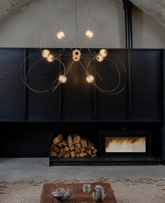 Modern chandelier hanging above a fireplace with firewood and a small table with items.