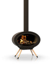A modern black freestanding wood burning fireplace with a visible fire inside, supported by three angled light wood legs, and a tall black chimney pipe extending upward against a white background.