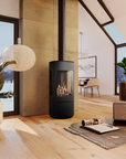 A modern black round gas fireplace with a glass front and visible flames, set in a bright, contemporary loft-style living room with light wood floors, plants, and a laptop on a rug.