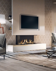 A modern linear gas fireplace with a white base and a black firebox insert, mounted on a beige wall beneath a flat-screen TV. The fireplace is set in a contemporary living room with patterned wallpaper, a gray sofa, a floor lamp, and a striped area rug.