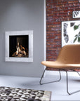A modern wall-mounted gas fireplace with a light gray textured surround and visible flames, shown in a styled interior with a tan lounge chair, brick wall, and patterned rug.