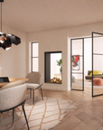 A modern dining area with a round wooden dining table, upholstered dining chairs, a black geometric pendant light, and a light beige patterned rug on a herringbone wood floor. In the background, a glass partition door looks into a living room with a gas fireplace and a sofa.