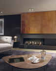 A modern living room interior featuring a black gas fireplace with visible flames, a large wood-paneled wall, a white sofa, a round wooden coffee table with cups and a moka pot, and a dark rug.