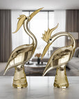 Two gold bird sculptures on a table with a modern living room in the background