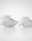 Two clear crystal seashell-shaped bowls with textured, ribbed interiors, displayed side-by-side on a light gray reflective surface.