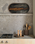 An oval tray with a dark marbled pattern and warm gold-brown center, displayed in a modern kitchen setting above a stone-topped counter with wooden utensils and a gas stovetop.