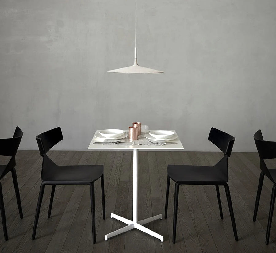 Modern dining setup with a white table and black chairs against a gray wall.