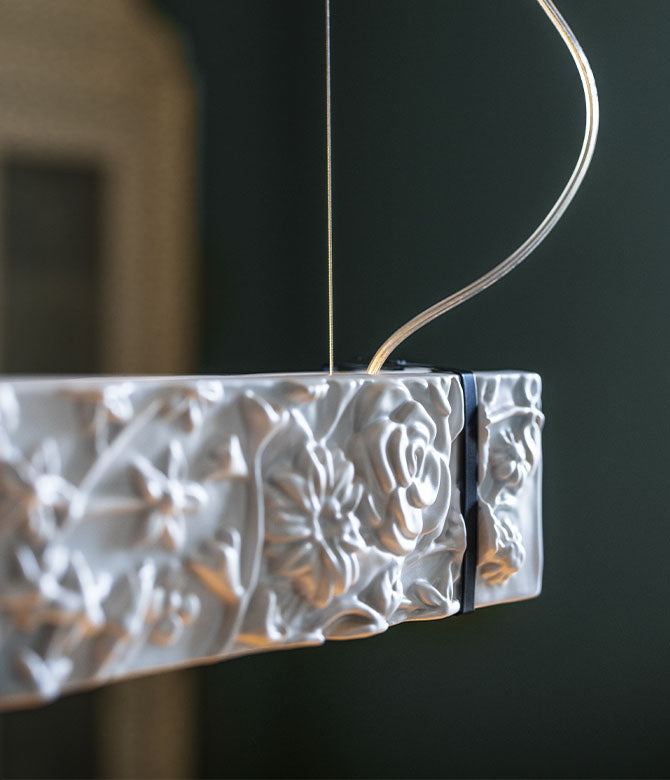 Decorative white ceramic suspension lamp with floral patterns hanging against a dark background