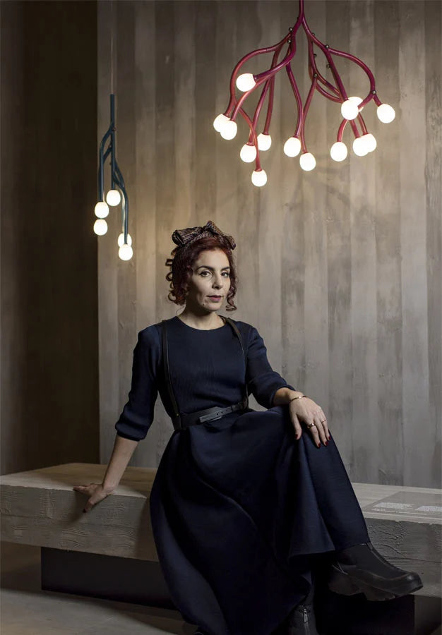 Woman in a dark dress sitting on a bench with modern chandeliers hanging above.