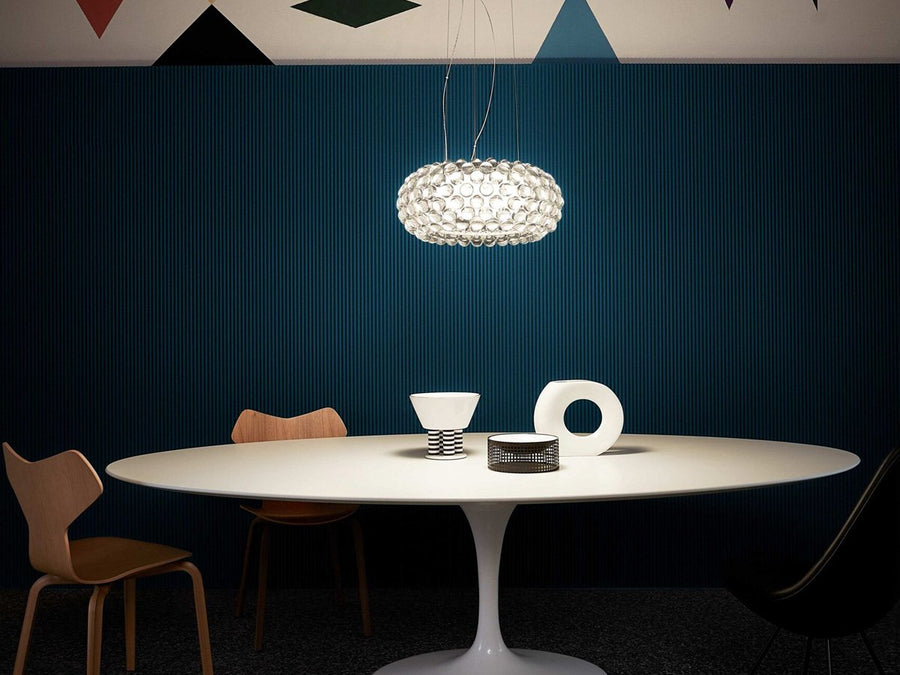 Modern dining room with a round table, chairs, and a hanging light fixture against a dark blue wall.