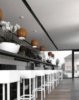 Modern interior with black tiled wall, white bar stools, and decorative ceiling lights.