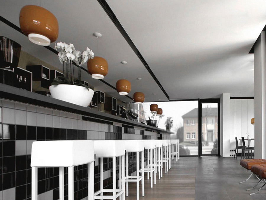 Modern interior with black tiled wall, white bar stools, and decorative ceiling lights.