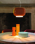 Round wooden table with orange pendant light and decorative items in a room with a fireplace.