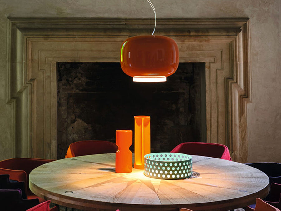 Round wooden table with orange pendant light and decorative items in a room with a fireplace.