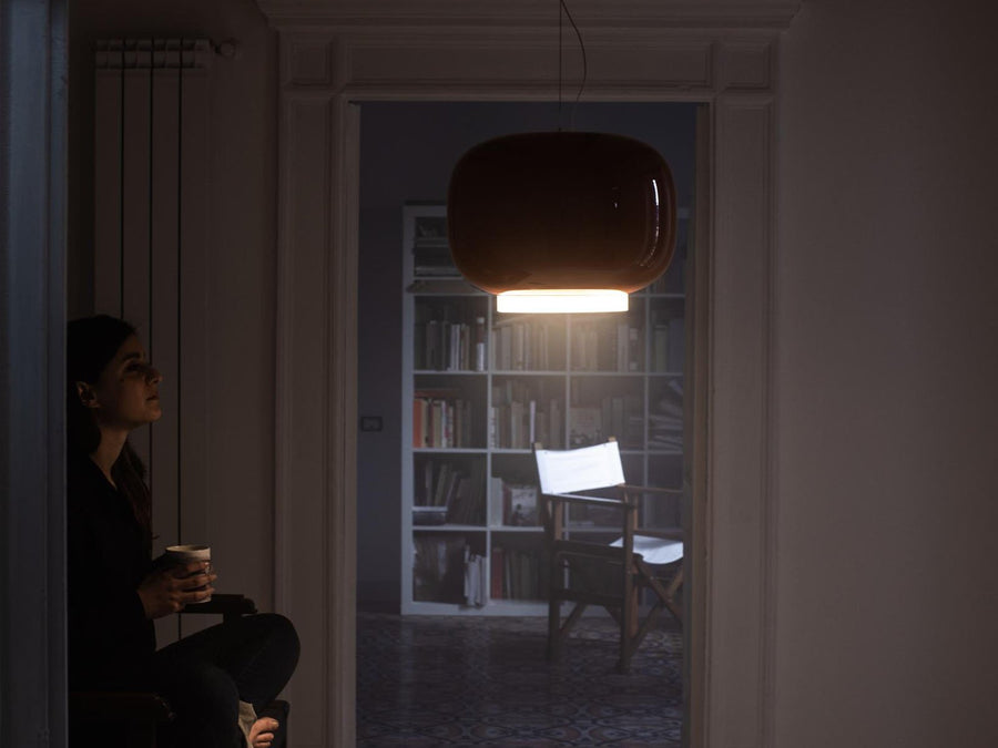 Person sitting in a dimly lit room with a bookshelf in the background