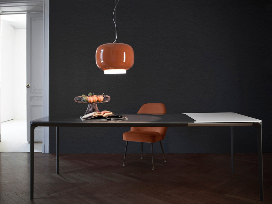 Modern office setup with a desk, chair, and pendant light against a dark wall.