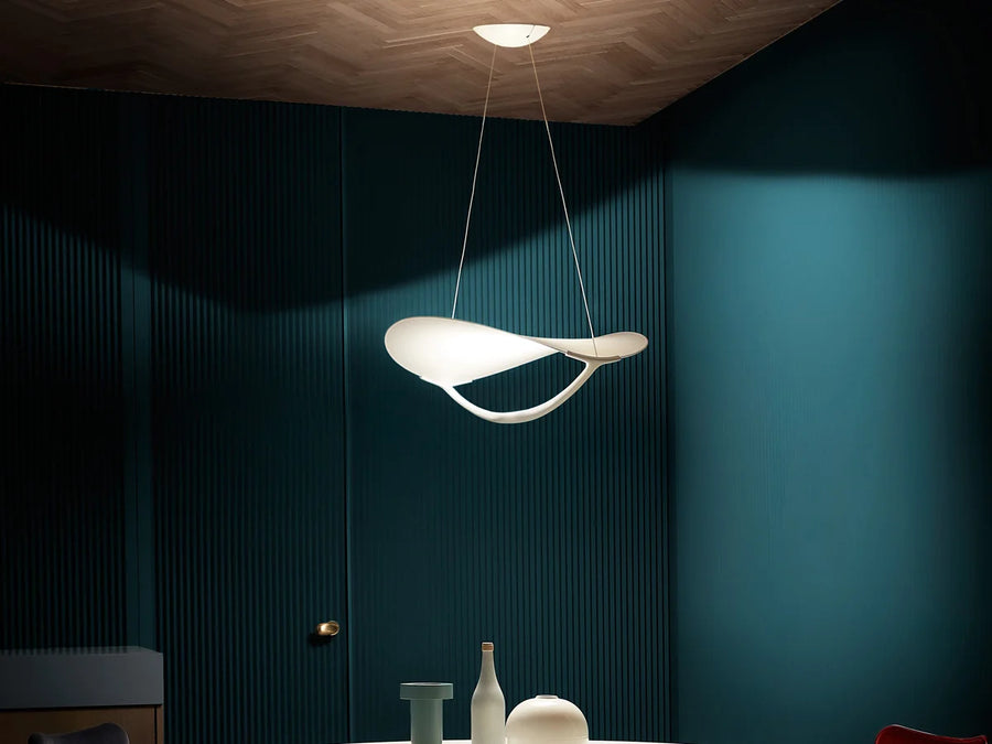 Modern pendant light hanging in a room with dark blue walls and decorative items on a table.