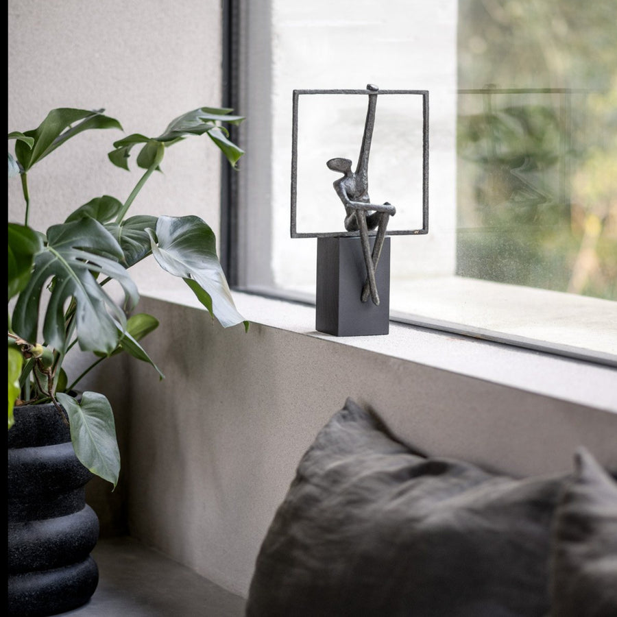 Decorative sculpture on a windowsill with a plant and cushions in the foreground.