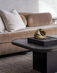 Modern living room with a beige sofa and a black coffee table featuring a gold finish bronze sculpture. 