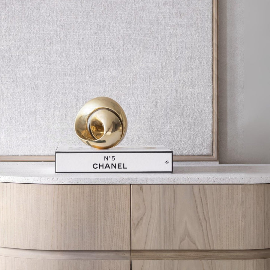 Decorative Chanel No. 5 bottle cap on a wooden surface with a textured wall background with a bronze sculpture