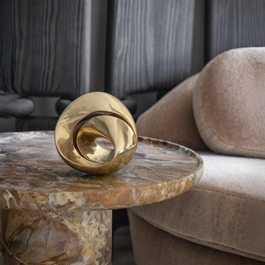 Gold decorative brass sculpture on a marble side table with a sofa in the background