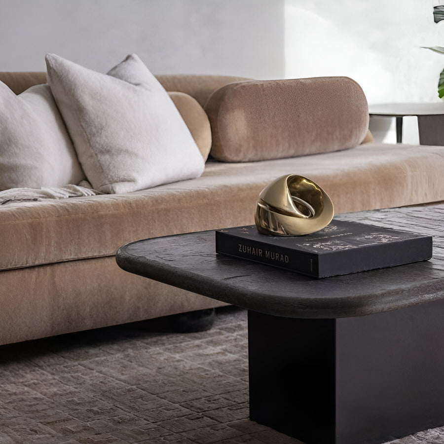 Modern living room with a beige sofa and a black coffee table featuring a gold finish bronze sculpture. 