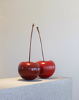 Two red cherries on a light gray surface with a neutral background