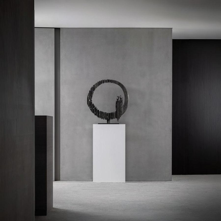 Modern sculpture on a pedestal against a gray wall in a minimalistic setting