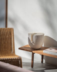 Wicker chair next to a wooden side table with a decorative sculpture from Gardeco and book against a white wall.