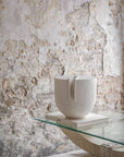 White ceramic sculpture on a glass table against a textured stone wall