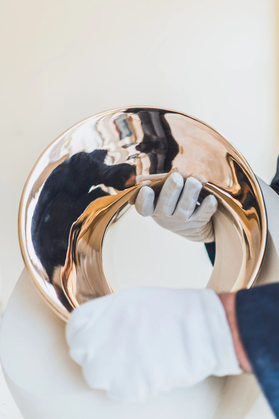 Gold decorative item being held by a person wearing gloves on a light background