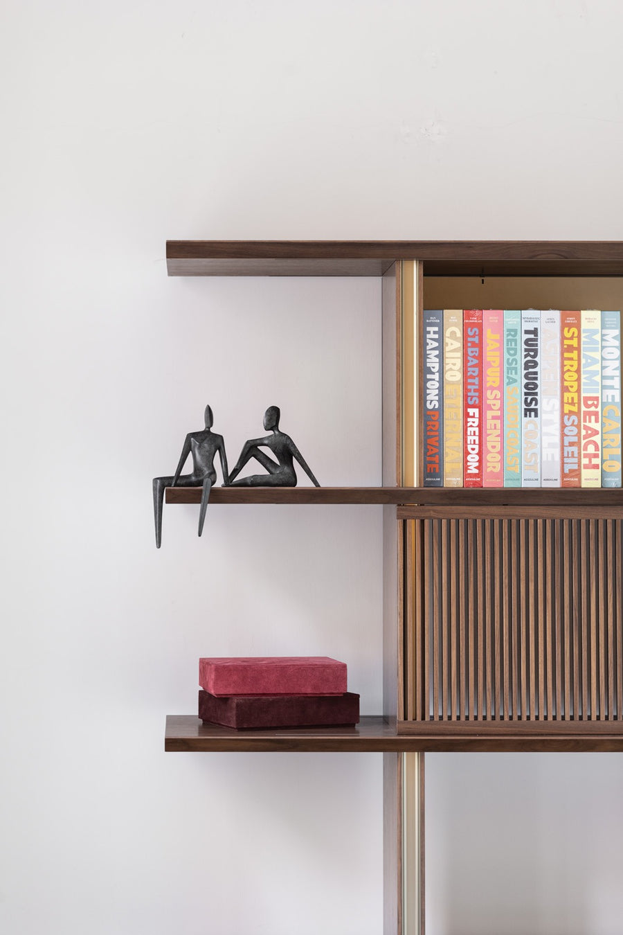 Wooden bookshelf with Assouline travel series cofffee table books & bronze sculptures from Gardeco against a white wall