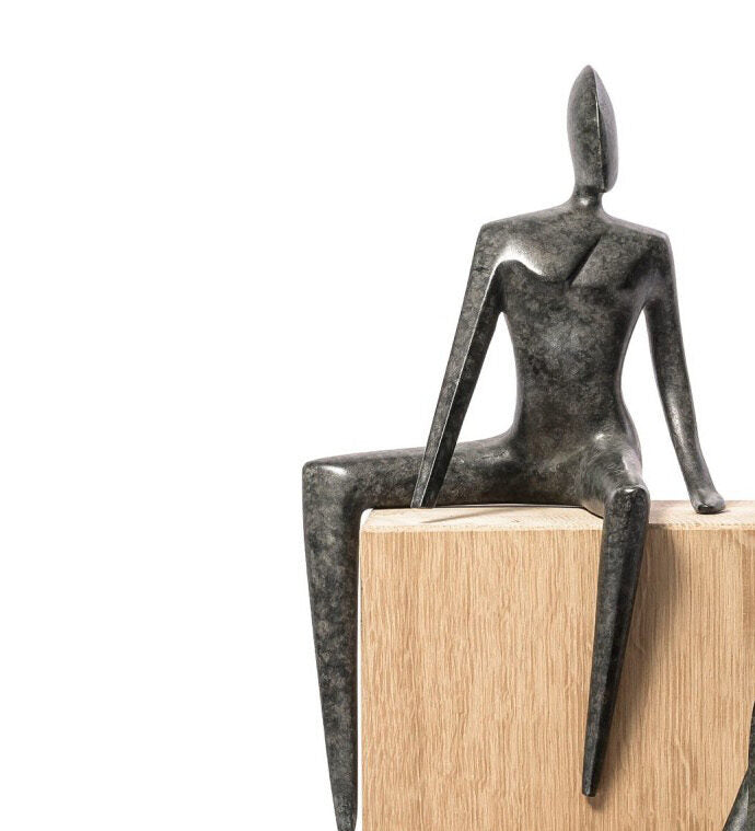Bronze sculpture of a seated figure on a wooden base against a white background