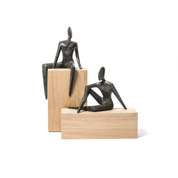 Two bronze sculptures of seated figures on wooden plinths against a white background