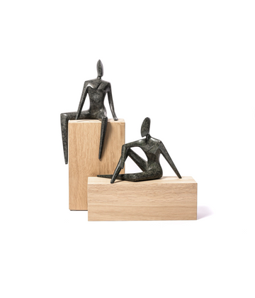 Two bronze sculptures of seated figures on wooden plinths against a white background