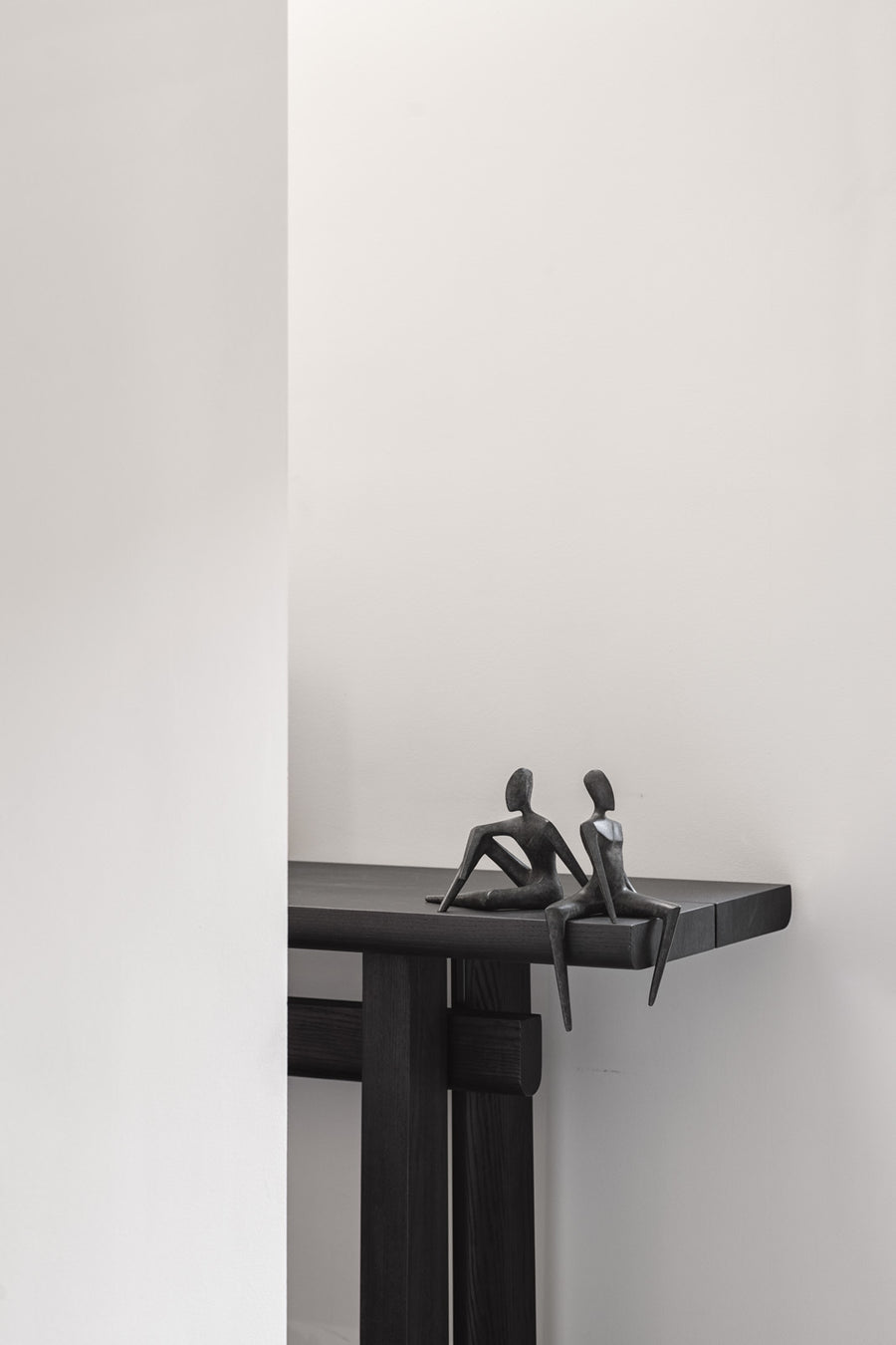 Two black sculptures of people sitting on a ledge against a white wall.