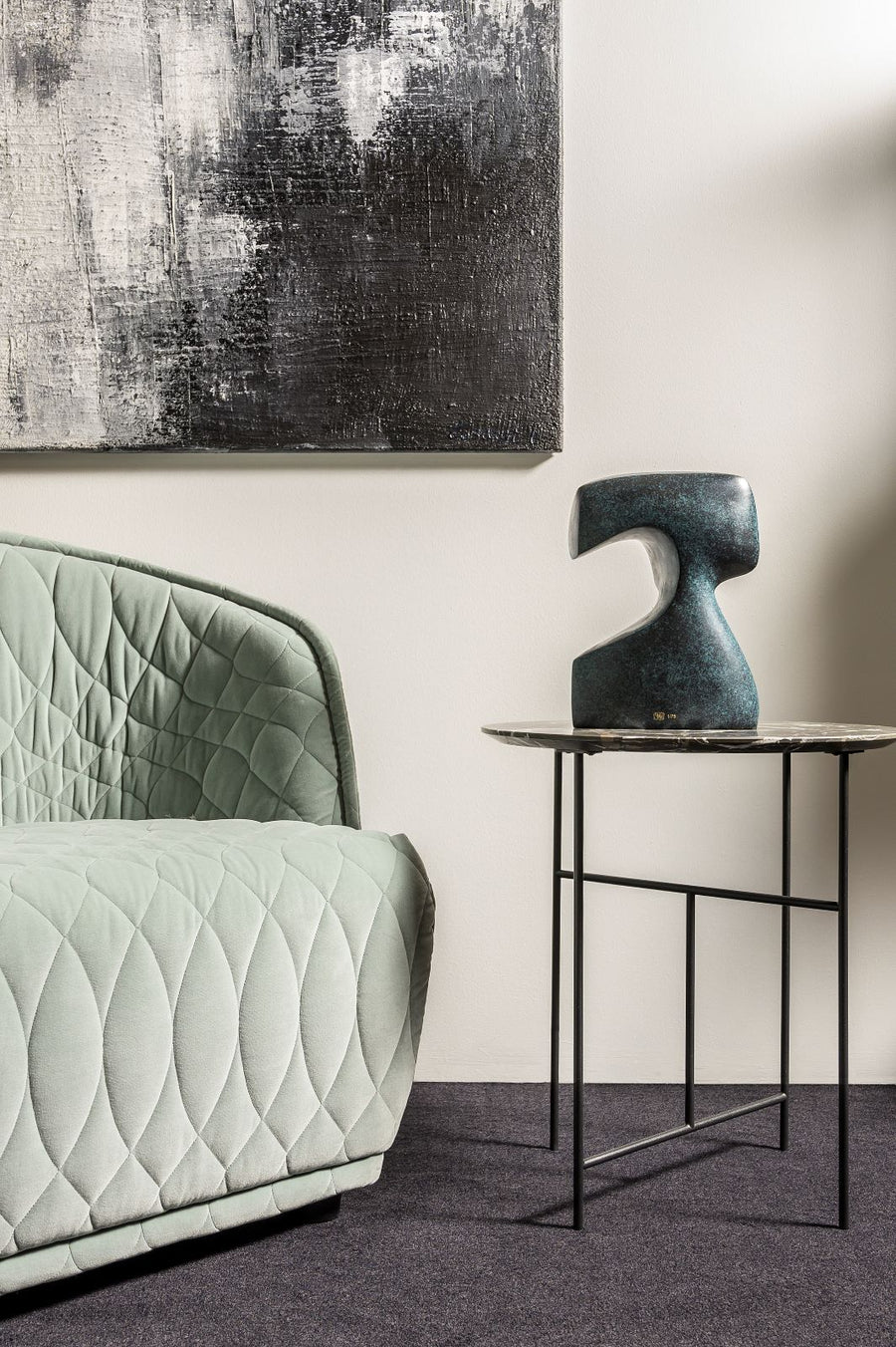 Modern interior with a quilted green sofa, abstract painting, and side table with sculpture.