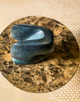 Blue green patina finish bronze sculpture on a circular marble-like surface with a beige background