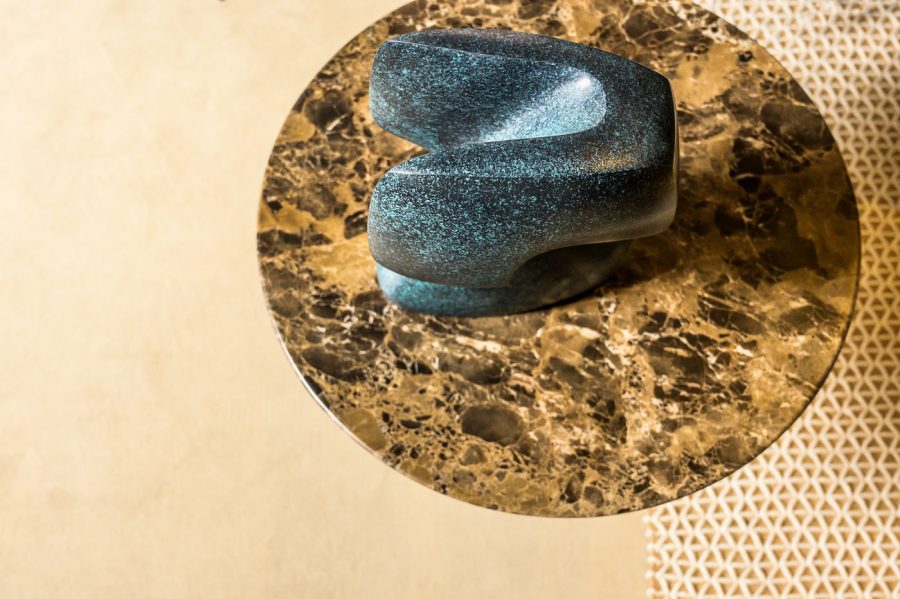 Blue green patina finish bronze sculpture on a circular marble-like surface with a beige background