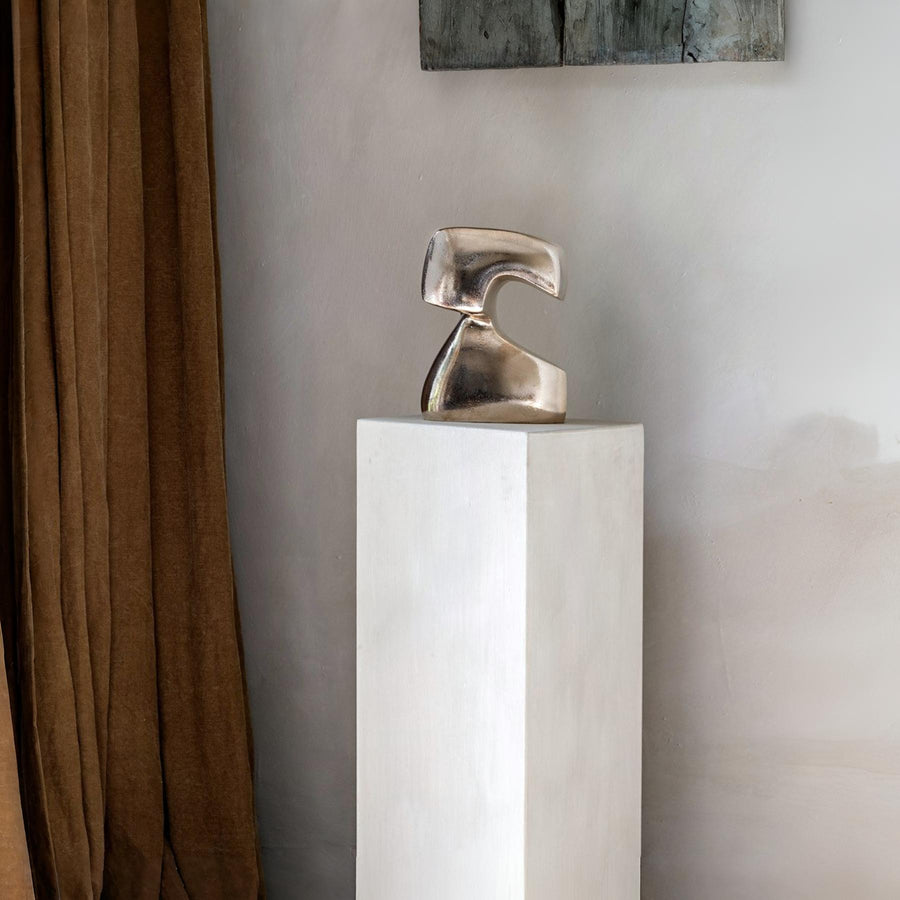 Bronze polished sculpture on a white pedestal against a neutral wall.