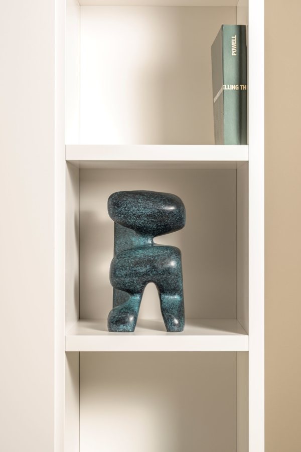 Blue abstract sculpture on a white shelf against a beige wall