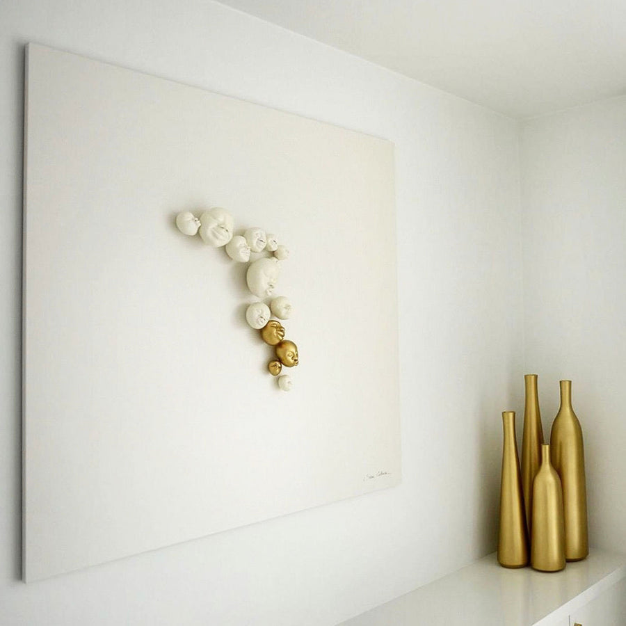 A white shelf adorned with a stunning Gardeco Happy Faces Wall Sculpture, created by renowned Brazilian ceramist Selma Calheira. The Gardeco Wall Sculpture Happy Faces features captivating white ceramic faces, beautifully.