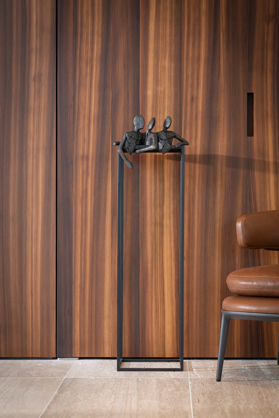 Decorative sculpture from Gardeco called Lets Talk on a stand against a wooden panelled wall with a chair partially visible.