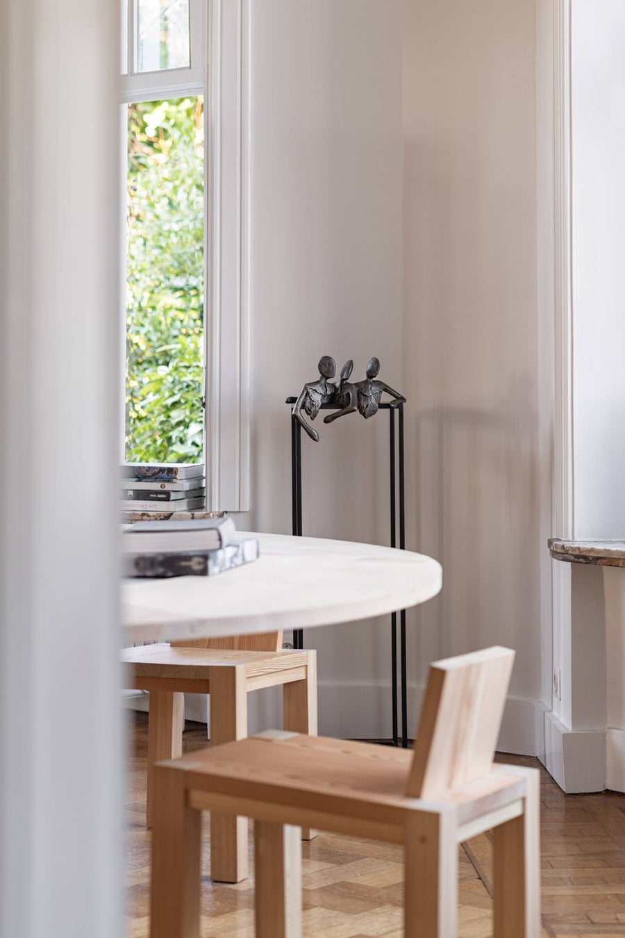 Dining area with a round white table and wooden chairs near a window and bronze sculpture of 3 men called Let's talk from Gardeco